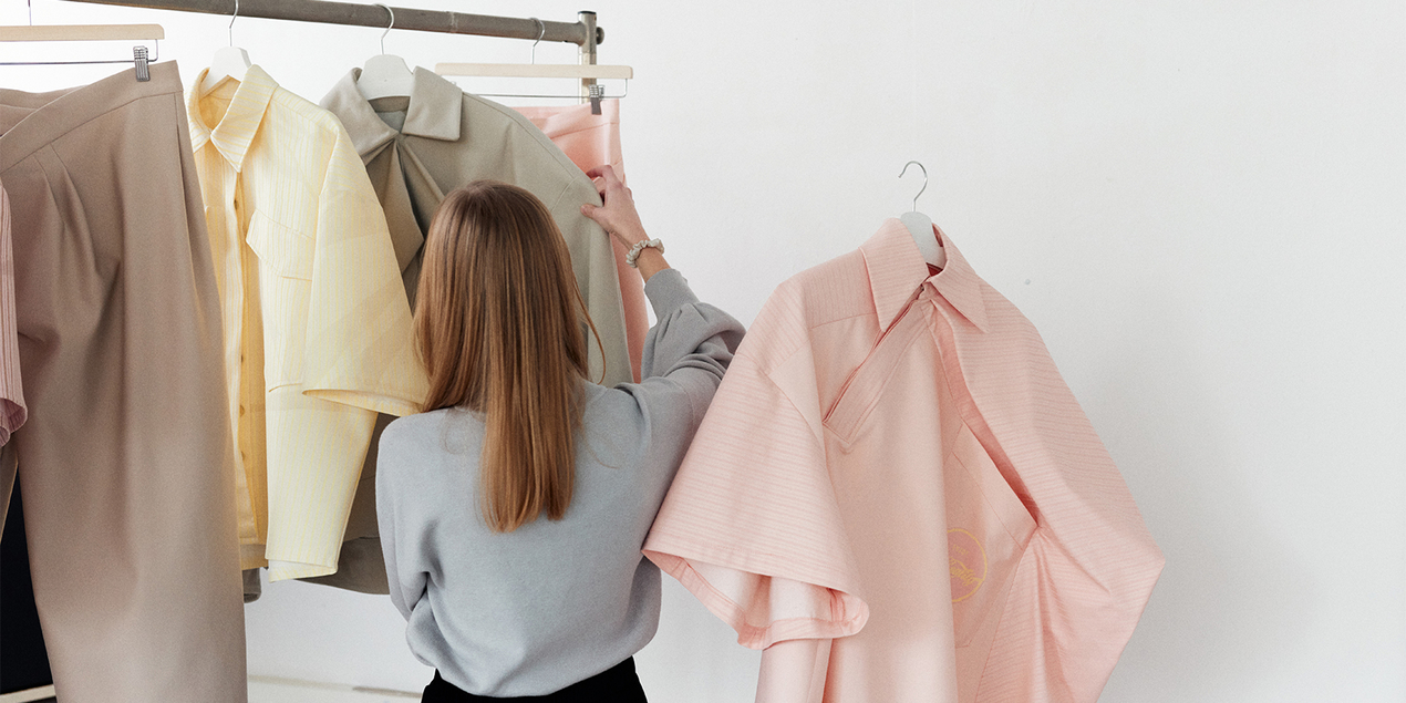 Eine Frau betrachtet Kleidungsstücke, die an einer Kleiderstange hängen.