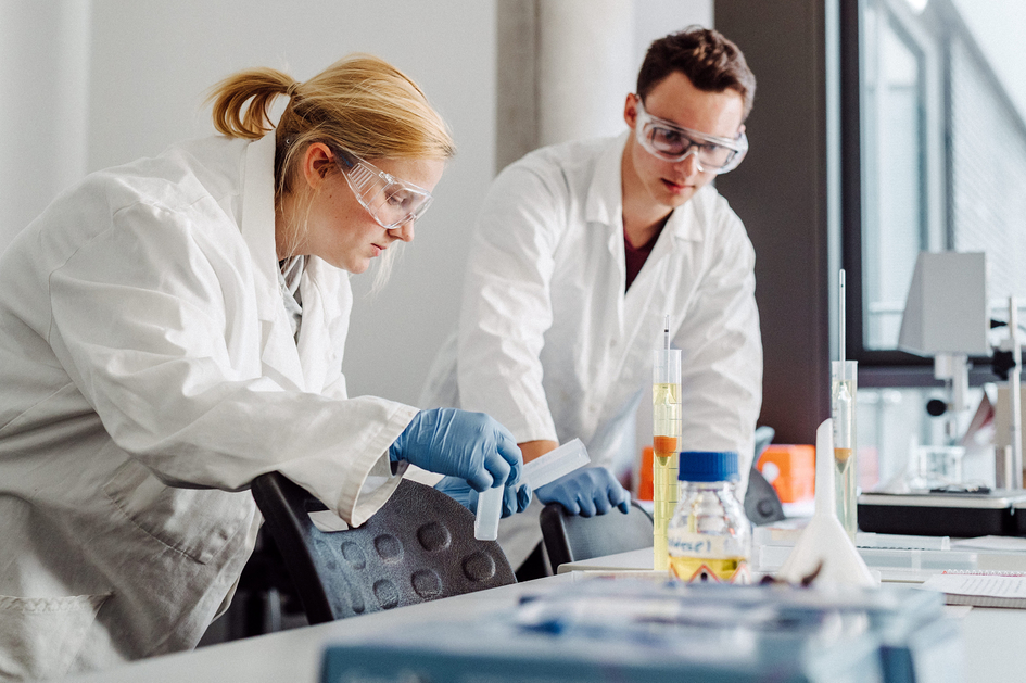 Eine Frau und eine Mann mit Schutzbrillen arbeiten mit Flüssigkeiten in einem Labor für Biochemie/Mikrobiologie